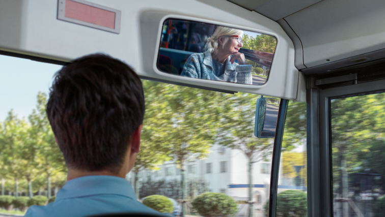 conducteur de bus regarde son rétroviseur dans lequel une femme passagère profite de son voyage paisiblement