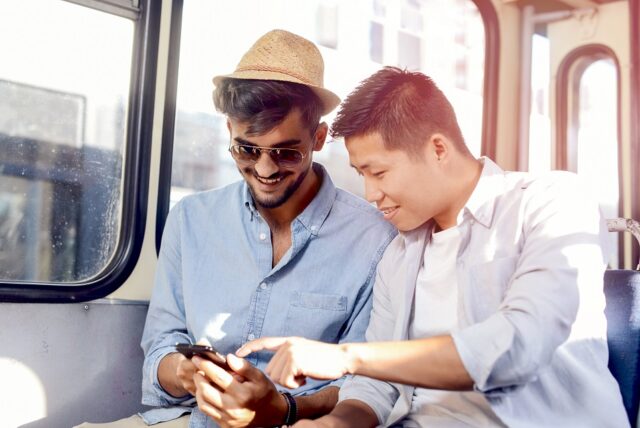 Deux jeunes hommes assis dans un bus regardent un smartphone