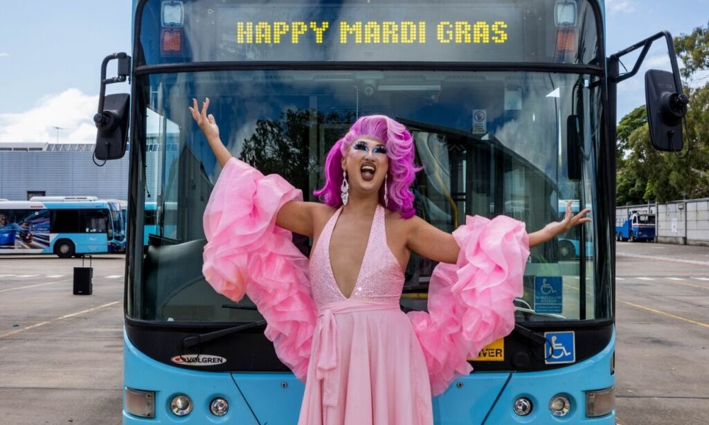 Drag Queen in pink dress standing in front of a Happy Mardi Gras bus in Sydney